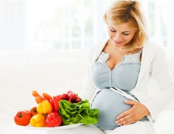 pregnant woman standing next to a bowl of vegetables